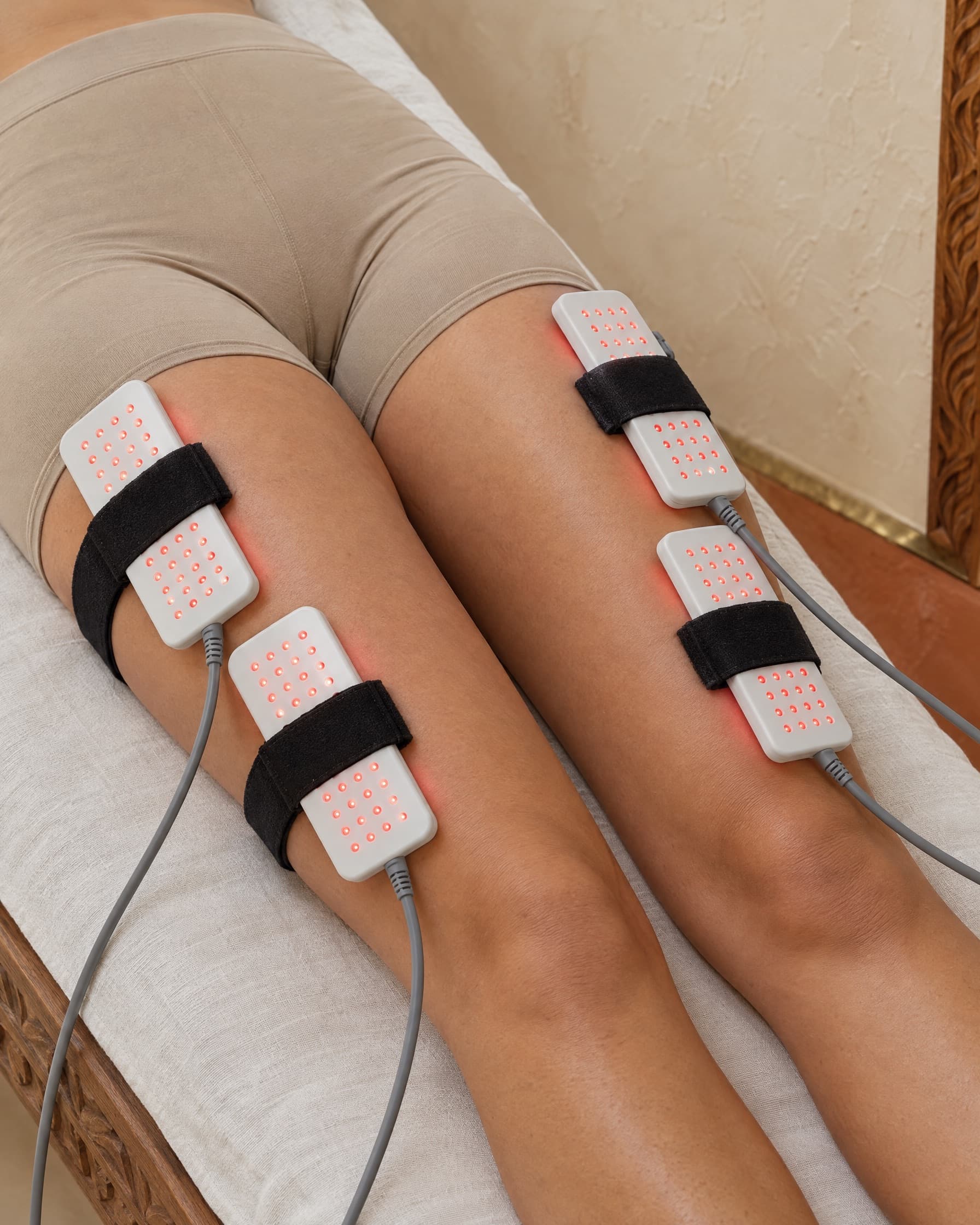 Red light laser lipo paddles strapped around a client's thighs on a linen-covered treatment bed