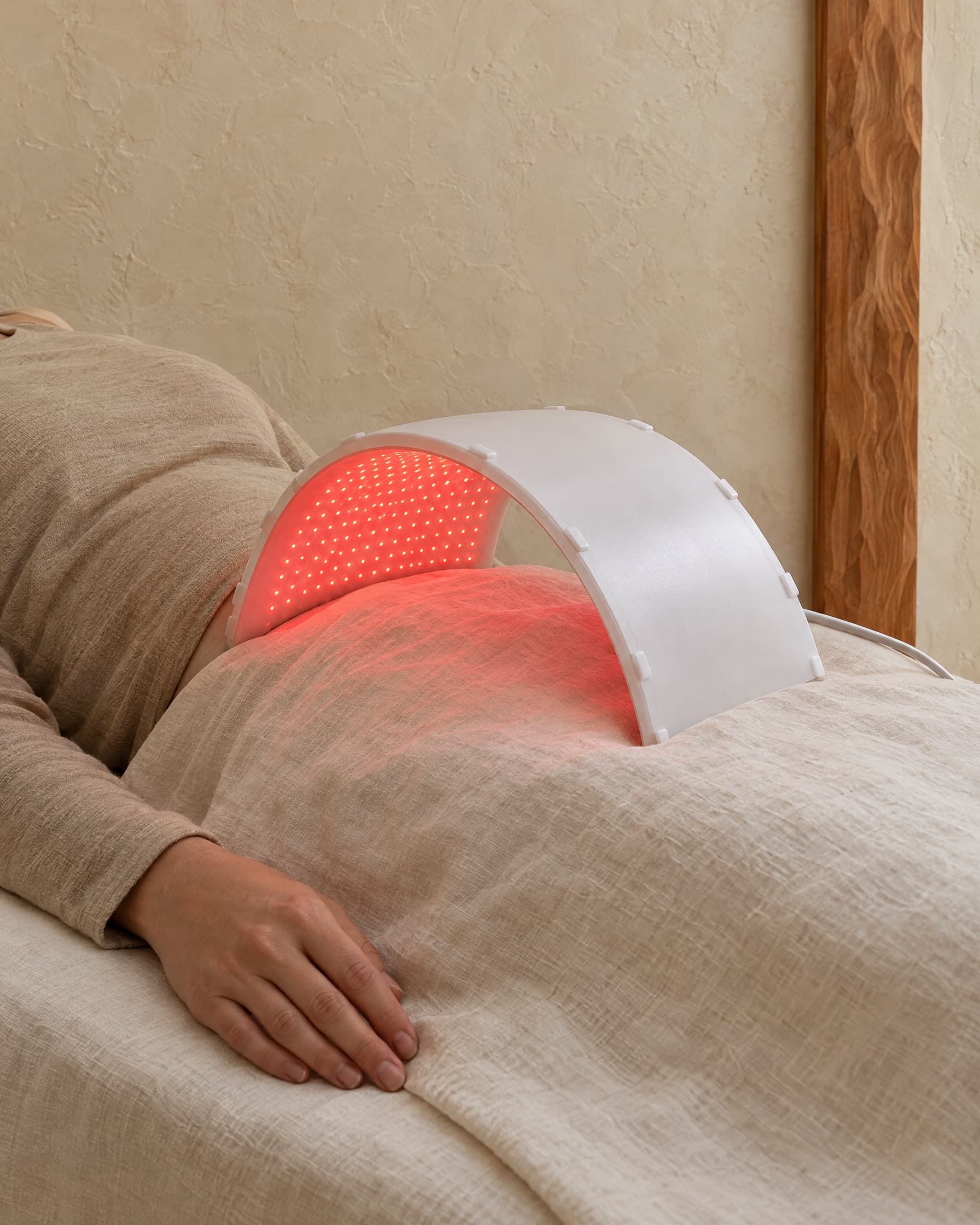 A curved LED light-therapy panel glowing red over a client's midsection under a linen sheet