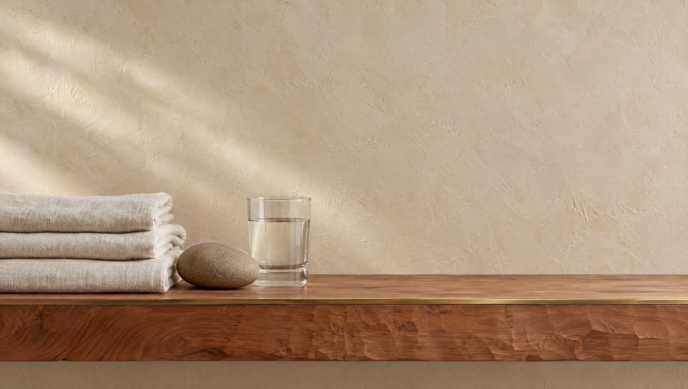 Folded linen towels, a smooth stone and a glass of water on a carved cedar ledge against plaster