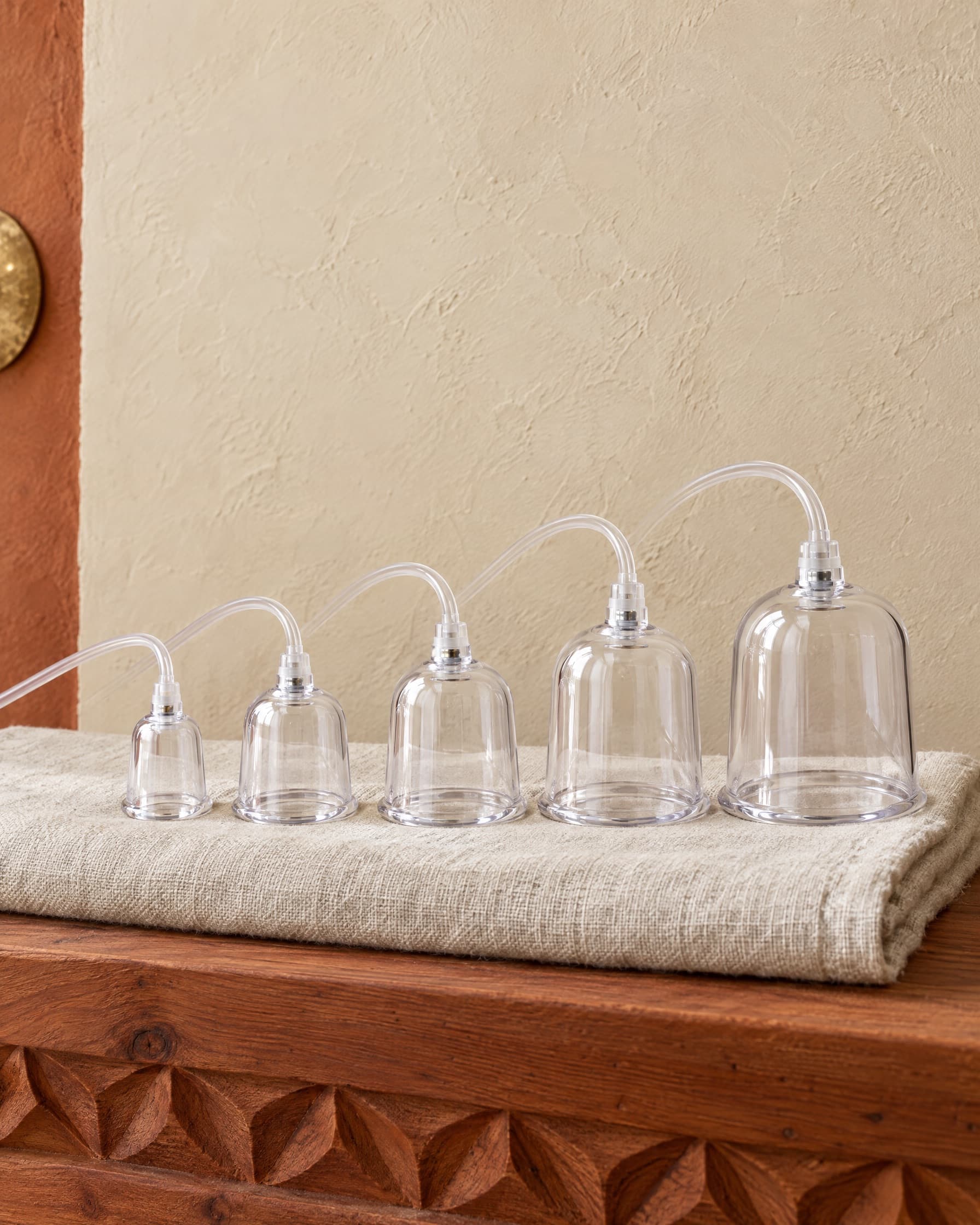 Clear acrylic vacuum therapy cups, small to large, on a folded linen towel on a carved cedar ledge